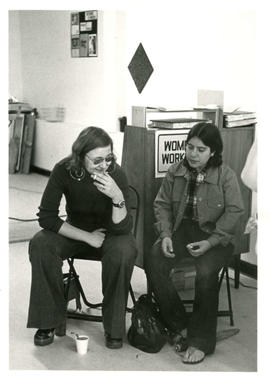 Two unidentified women sitting on chairs with a cup of coffee at their feet