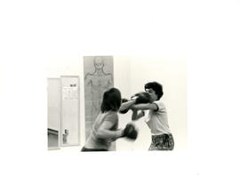 Side view of two women boxing with drawing of a person in the background  at the Amazon Self-Defe...