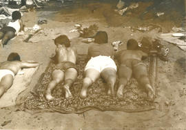 Five women lying down on blankets at the beach with their back to the camera